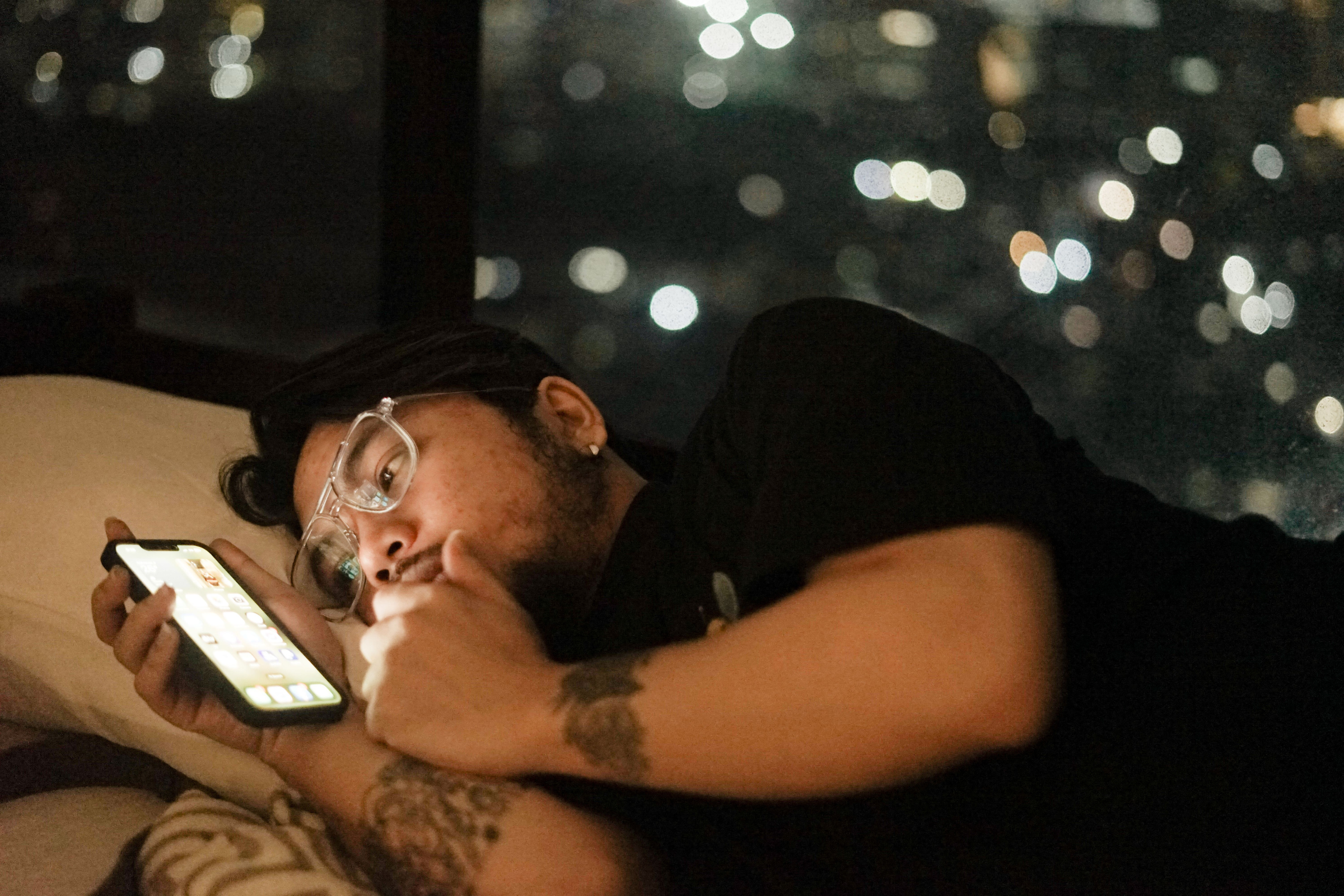 Young Indian man lying awake at night looking at his phone