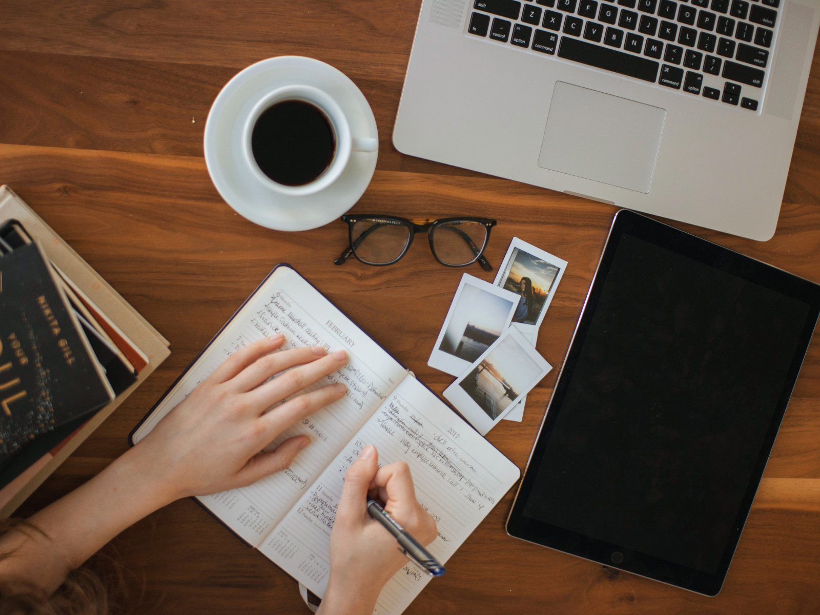 Person writing in a journal beside a laptop and coffee